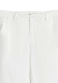 Pantalons blancs avec une texture lisse, dotés d'une fermeture à bouton à l'avant et d'un design plat à l'avant. Détails minimaux, adaptés pour un style polyvalent.