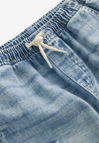 Shorts de mezclilla azul claro con cinturilla elástica, bolsillos frontales y un acabado suave y deslavado, con una textura ligeramente desgastada.