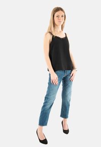 Top de tirantes negro con encaje, de tela ligera, combinado con jeans rectos de un azul medio, usado con tacones negros de punta. Estilo de outfit casual.