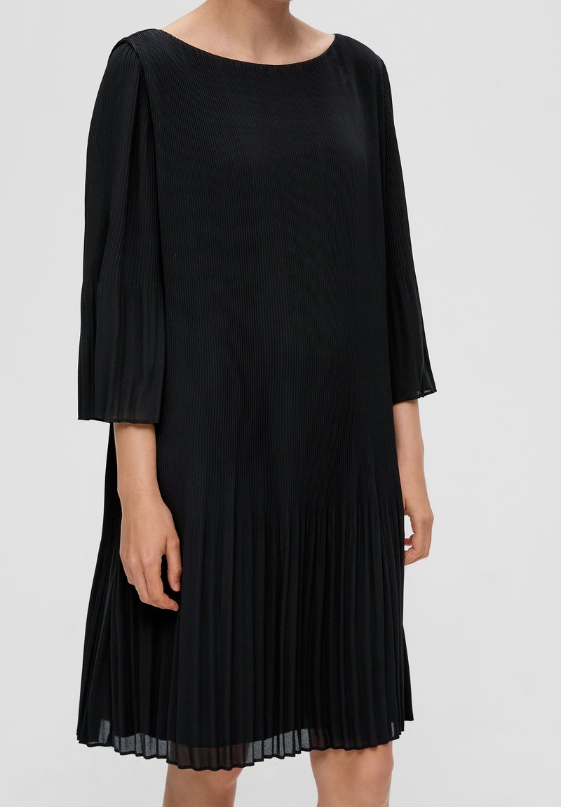 Svart plisserad klänning med trekvartslånga ärmar, med rund halsringning och en texturerad ribbad design, som faller strax ovanför knäna.