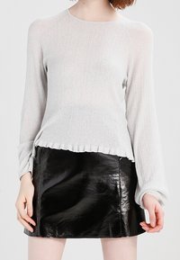 Person trägt ein hellgraues, geripptes Langarmshirt mit gerüschtem Saum und einen glänzenden schwarzen Leder-Minirock.