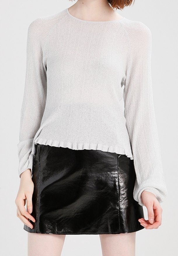 Person trägt ein hellgraues, geripptes Langarmshirt mit gerüschtem Saum und einen glänzenden schwarzen Leder-Minirock.