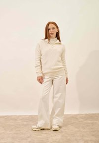 Biały sweter dziany z zamkiem przy kołnierzu i wzorem w diamenty, w połączeniu z szerokimi, białymi spodniami i beżowymi sneakersami. Gładka faktura.