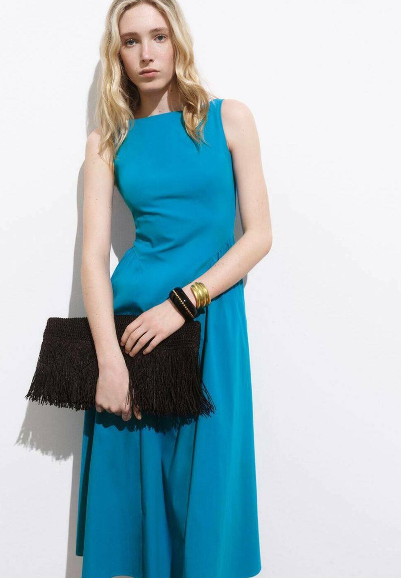 Rochie fără mâneci de culoare turcoaz, cu corset ajustat și fustă evazată. Clutch cu franjuri negre și brățări aurii. Material neted, design minimalist.