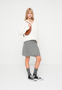 Maglione color crema, gonna grigia a trama, sneakers nere e calze grigie. Borsa a tracolla marrone dalla forma ricurva. Design semplice, stile casual.