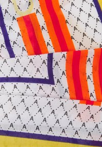 Tessuto colorato a motivi con strisce diagonali arancioni, rosse e viola, caratterizzato da lettere 'A' nere ripetute su uno sfondo bianco.