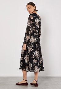Schwarzes Blumenkleid mit langen Ärmeln, tailliert, aus einem weichen Stoff und lebendigen Blumennmustern in Rosa- und Cremetönen.