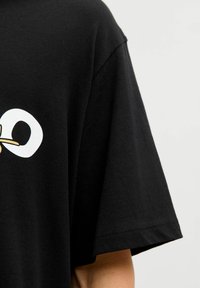 Czarny bawełniany t-shirt o luźnym kroju z białym graficznym nadrukiem logo i złotym akcentem. Krótkie rękawy i okrągły dekolt.