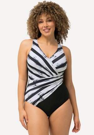 Mujer con cabello rizado sonriendo, con un bañador de una pieza a rayas negras y blancas con diseño envolvente.