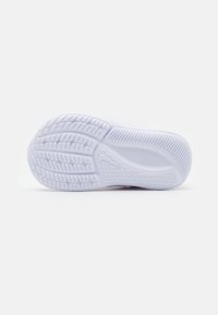 Suela de zapatilla blanca con suela de goma texturizada que presenta patrones curvos y pequeñas ranuras para tracción. Superficie suave con detalles sutiles.