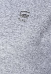 Šedé bavlněné tričko se subtilním vyšitým logem s nápisem "RAW" a geometrickým vzorem. Měkká textura a pohodlný střih.