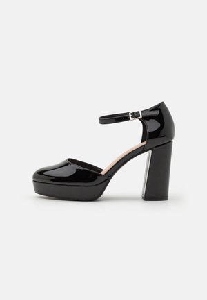 Black patent leather platform heels with an ankle strap, round toe, and a chunky square heel, featuring a glossy finish and clean lines.