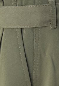Olivově zelená látka s hladkým povrchem, s širokým páskem a sklady, které zdůrazňují strukturovaný design a odolné švy.