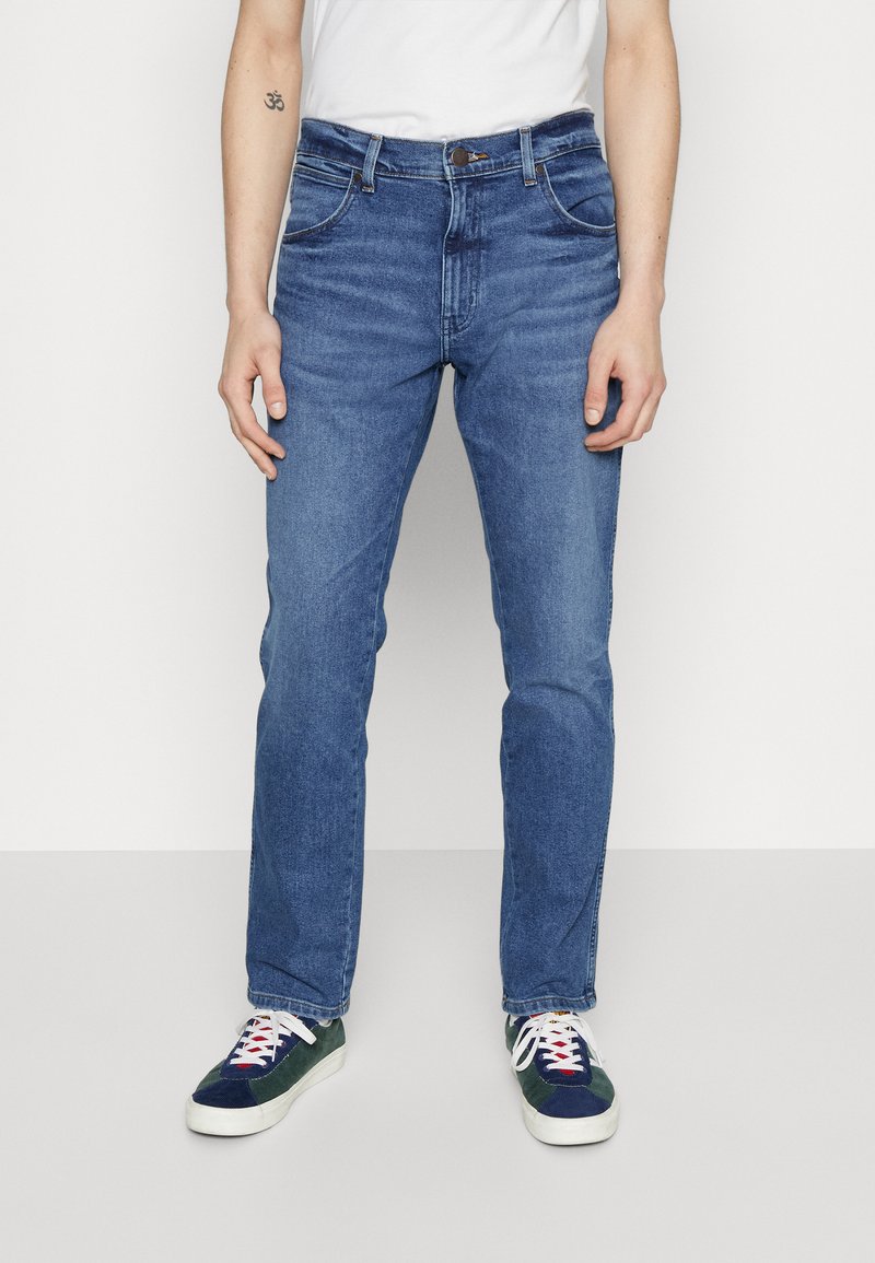 Vaqueros de mezclilla azul con diseño de pierna recta, estilo de cinco bolsillos y cierre de botones clásico. Llevados con zapatillas multicolores.