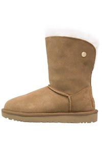 Bottine en daim marron avec un bout arrondi, doublure en fourrure blanche douce au sommet et un bouton décoratif doré. Semelle en caoutchouc plate.