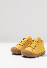 Scarpe per bambini in pelle gialla con punte tonde, lacci tonali e suole in gomma con finitura testurizzata. Nessun logo o motivo visibile.