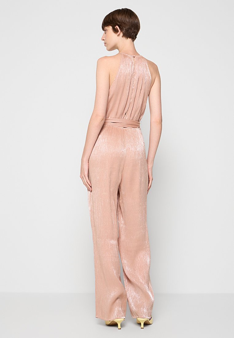 Blush-pink Jumpsuit mit seidig-glatter Textur, weitem Bein und Halterneck. Mit einem taillierten Gürtel und subtilen vertikalen Falten am Rücken.
