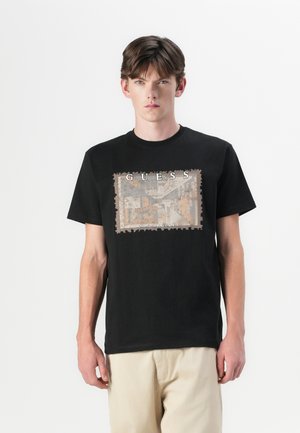 Zwarte katoenen t-shirt met een vintage-stijl grafische print in beige en bruin, omrand met een postzegelachtige ontwerp.