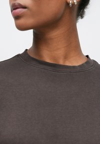 Σκούρο καφέ βαμβακερό φούτερ με στρογγυλή λαιμόκοψη και ορατές ραφές. Ομαλή υφή, χωρίς σχέδια ή επιπλέον διακοσμητικά.