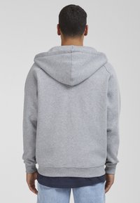Gray cotton hoodie with a large, soft hood, ribbed cuffs, and hem. Smooth texture with a relaxed fit, worn over a navy shirt.