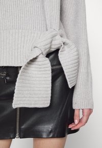 Grå ribbstickad tröja med en knutdetalj i sidan, kombinerad med en svart läderminikjol med en synlig dragkedja.