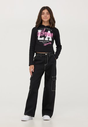 Crop hoodie nera con la scritta "CALIFORNIA" e "LA" in rosa. Abbinato a pantaloni cargo neri con cuciture bianche e tasche. Sneakers bianche.