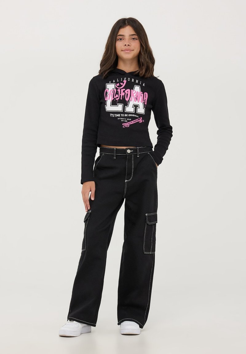 Crop hoodie nera con la scritta "CALIFORNIA" e "LA" in rosa. Abbinato a pantaloni cargo neri con cuciture bianche e tasche. Sneakers bianche.