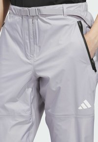 Pantalones deportivos de color gris claro con una textura suave, que cuentan con un bolsillo delantero con cierre, trabillas para cinturón y un pequeño logo blanco de la marca en la pierna.