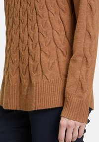 Brauner Kabelstrickpullover mit strukturiertem Muster, geripptem Saum und Ärmeln, aus weichem Wollmischgewebe, präsentiert mit dunklen Hosen.