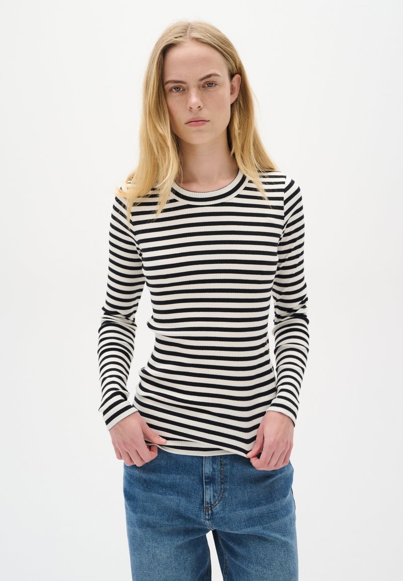 Striped long-sleeve top featuring a ribbed texture in black and white. Standard crew neckline, fitted design, paired with blue jeans.