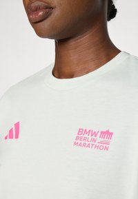 T-shirt verde menta chiara con scollo tondo. Presenta il logo rosa di Adidas e il testo "BMW BERLIN MARATHON" stampato sul davanti.