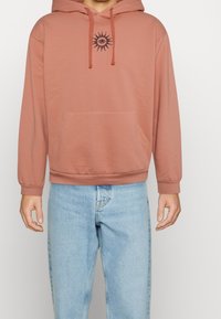 Felpa con cappuccio in tessuto rosa polveroso con tasca anteriore, caratterizzata da ricami neri di sole ed occhio sul petto. Maniche e orlo a costine.