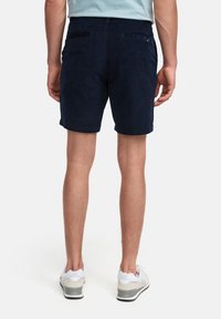 Marinen shorts i mjukt tyg, med två bakfickor, en vikta fåll och en figurnära midja. Bärs med ljusa sneakers.