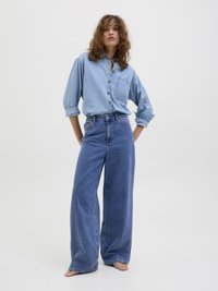 Svetlo modra denim srajca z dolgimi rokavi in žepom na prsih v kombinaciji z modrimi širokimi hlačami visokega pasu. Preprost dizajn, sproščen kroj.