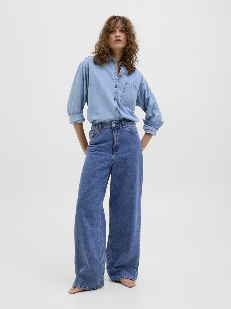 Svetlo modra denim srajca z dolgimi rokavi in žepom na prsih v kombinaciji z modrimi širokimi hlačami visokega pasu. Preprost dizajn, sproščen kroj.