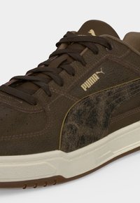 Καφέ δερμάτινο αθλητικό παπούτσι Puma με σκούρα καφέ κορδόνια, λευκή σόλα και χρυσό λογότυπο Puma στο πλάι και στη γλώσσα.
