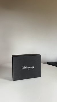 Caja rectangular negra con acabado mate, con el texto en cursiva blanca "Salinyang" en la parte frontal, colocada sobre una superficie blanca lisa.