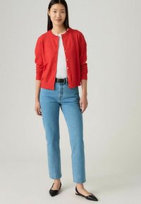 Cárdigan rojo con cuello redondo, cierre de botones y puños acanalados, combinado con jeans rectos de mezclilla azul claro y bailarinas negras de punta.