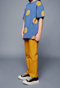 Camiseta de algodón azul con motivos de sol amarillos, combinada con pantalones de pana amarillos texturizados y zapatillas negras con suelas y cordones blancos.