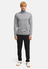 Hellgrauer Rollkragenpullover aus weichem Material, körpernahe Passform, mit gerippten Säumen an den Ärmeln und am Saum. Kombiniert mit schwarzen Hosen und weißen Sneakers.
