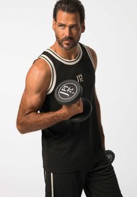 Canotta atletica nera con bordi bianchi, dotata di un logo; il modello tiene un manubrio nero, mostrando braccia toniche e un fisico muscoloso.