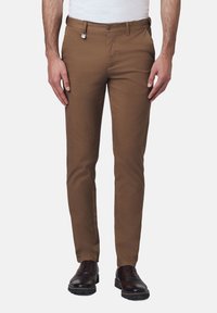 Brązowe bawełniane spodnie o dopasowanym kroju, z zapięciem na guzik, kieszeniami z przodu i mocnym splotem materiału. Pasują do brązowego obuwia.