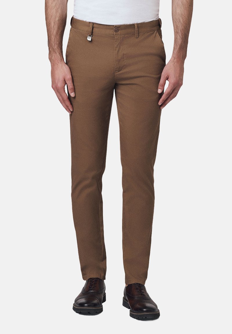 Brązowe bawełniane spodnie o dopasowanym kroju, z zapięciem na guzik, kieszeniami z przodu i mocnym splotem materiału. Pasują do brązowego obuwia.