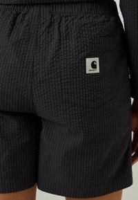 Donkergrijze shorts van gestructureerde stof met een subtiel ruitpatroon. Elastische tailleband en een achterzak met een wit logotag.
