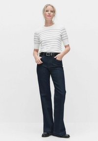 Hvid kortærmet top med marineblå striber, parret med mørkeblå flared jeans og et sort bælte. Glatte teksturer og klassisk design.