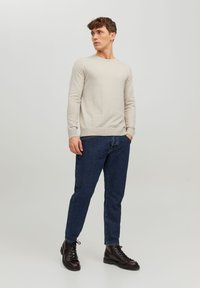 Light beige, long-sleeve sweater with a round neckline, paired with dark blue jeans and black lace-up boots. Smooth texture, casual fit.