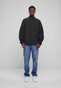 Svart overdimensjonert hettegenser med høy hals, sammen med lyseblå rette jeans og hvite sneakers. Enkelt, avslappet design og passform.