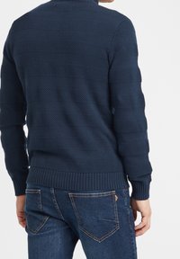 Maglione a maglia blu navy con motivo a texture e righe. Polsini e orlo a coste. Abbinato a jeans blu scuro.