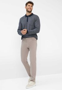 Langärmliges marineblaues Polo mit Tasche, kombiniert mit hellbeigen Slim-Fit-Hosen. Weiße Sneaker runden das Outfit ab.