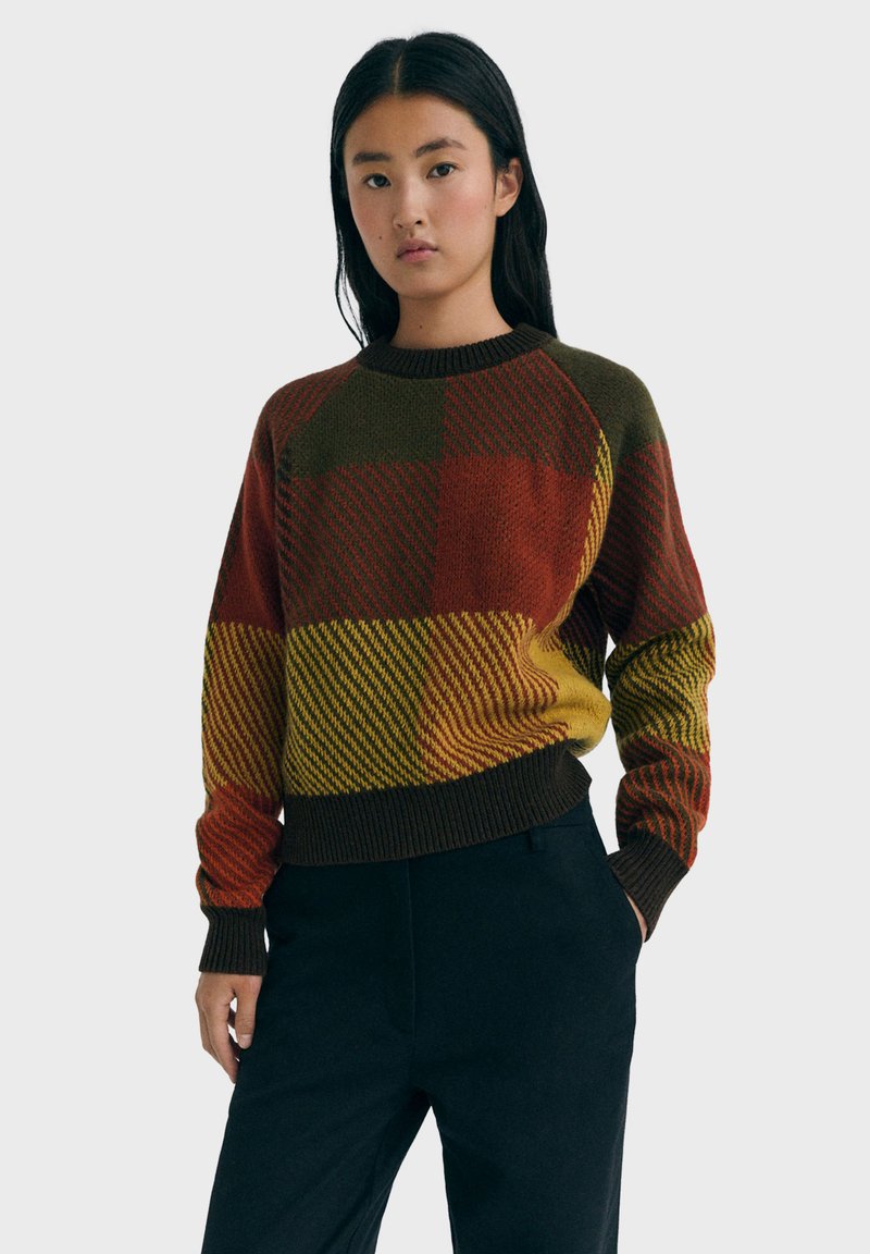 Pullover lavorato a maglia multicolore con motivo a quadri in tonalità di rosso, verde e giallo, con un colletto e polsini a coste marroni.
